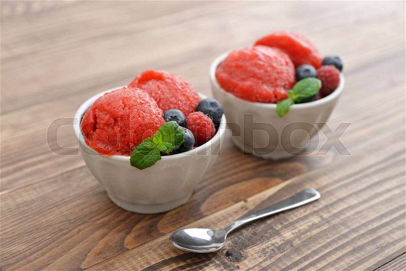 Fruit strawberry sorbet with raspberry, blueberry and mint in a bowl on wooden background, stock photo