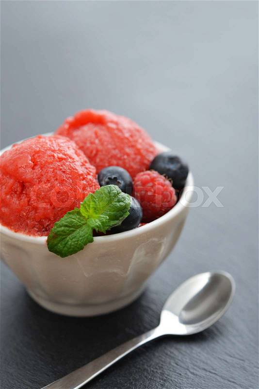 Fruit strawberry sorbet with raspberry, blueberry and mint in a bowl on black slate background, stock photo