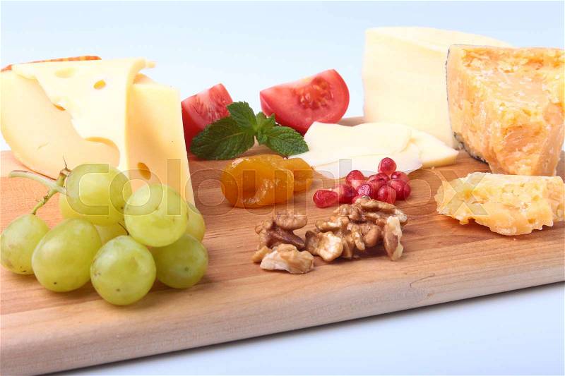 Assortment of cheese with fruits, grapes, nuts and cheese knife on a wooden serving tray, stock photo