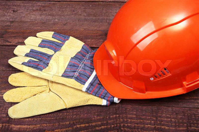 Orange hard hat and gloves for work on wood background, stock photo
