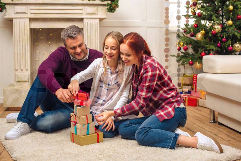 Happy family stacking christmas gifts while sitting on floor at home, stock photo