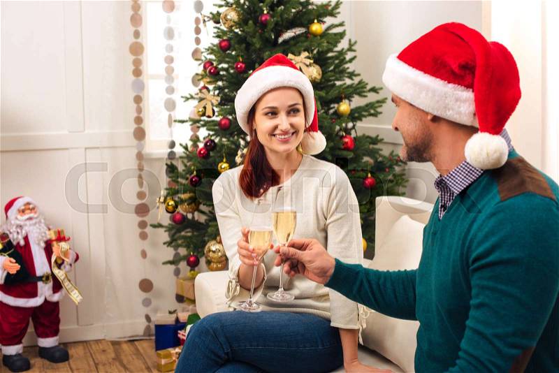 Happy couple in santa hats drinking champagne together at christmas eve, stock photo