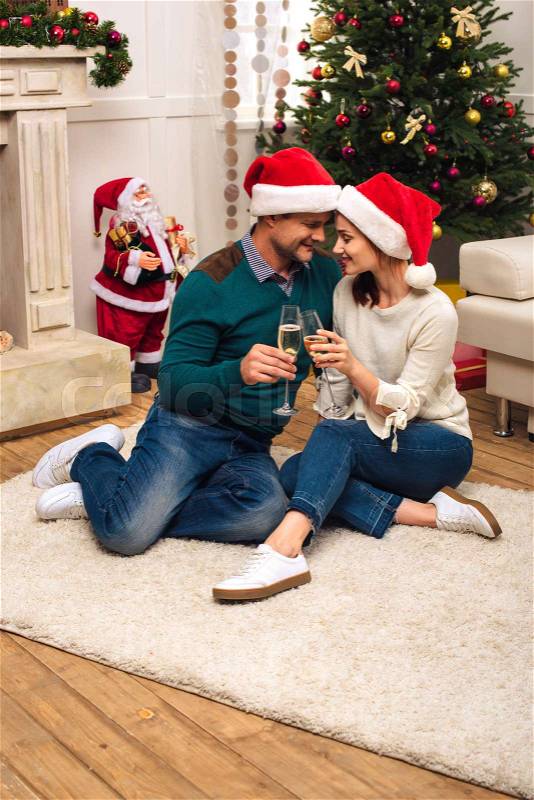 Couple drinking champagne while sitting together on carpet at new year party, stock photo