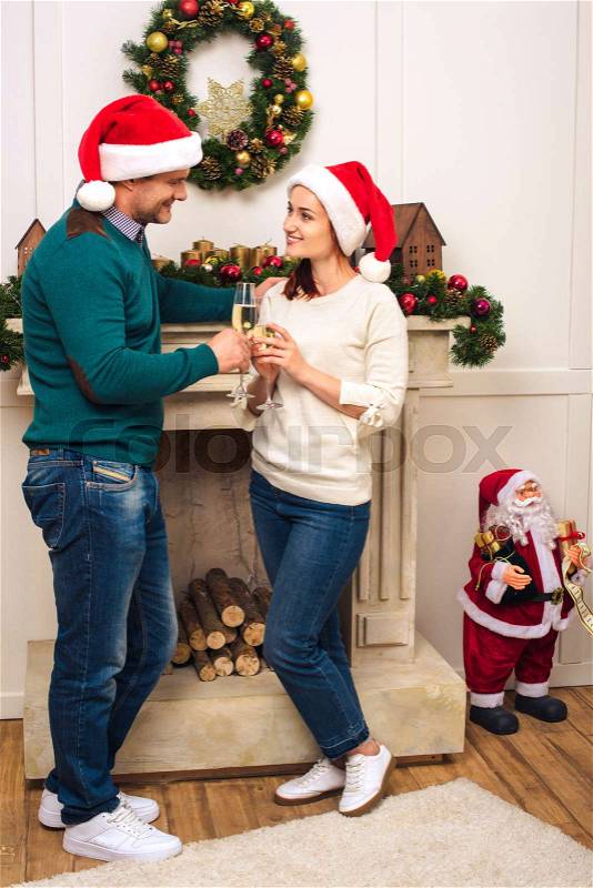Happy couple in santa hats drinking champagne and smiling each other at home, stock photo