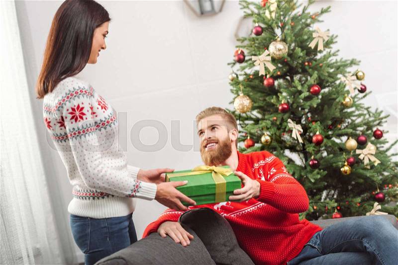 Beautiful smiling girl presenting christmas gift to happy boyfriend at home, stock photo