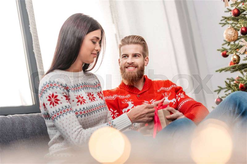 Handsome bearded man presenting christmas gift to happy girlfriend at home, stock photo