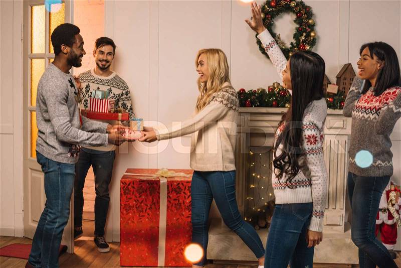 Multicultural men presenting christmas gifts to friends while celebrating gifts together, stock photo