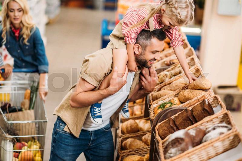 Smiling father and adorable little daughter buying bread in supermarket , stock photo