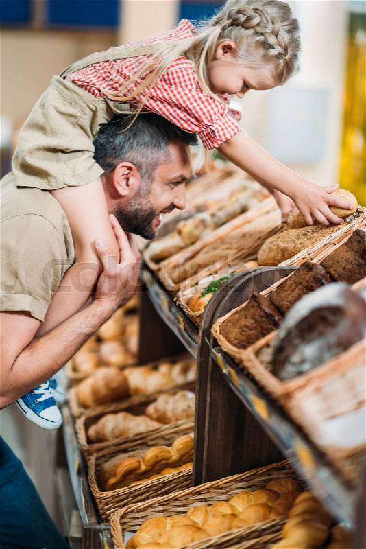 Side view of happy father and daughter buying bread in supermarket, stock photo