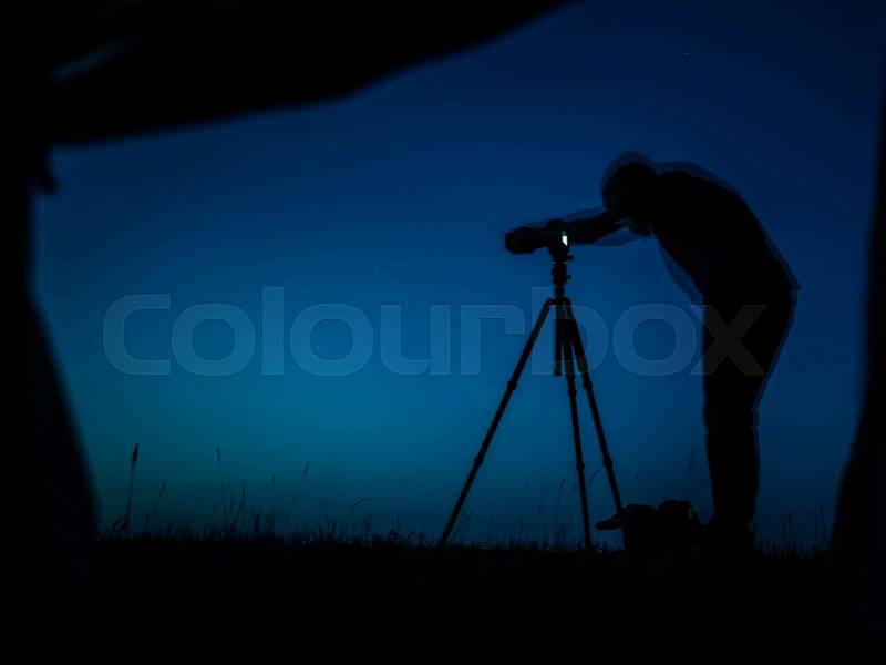 Artistic long exposure photo of a photographer in action. Multiple silhouettes and a camera un tripod. A view from a tent in night, stock photo