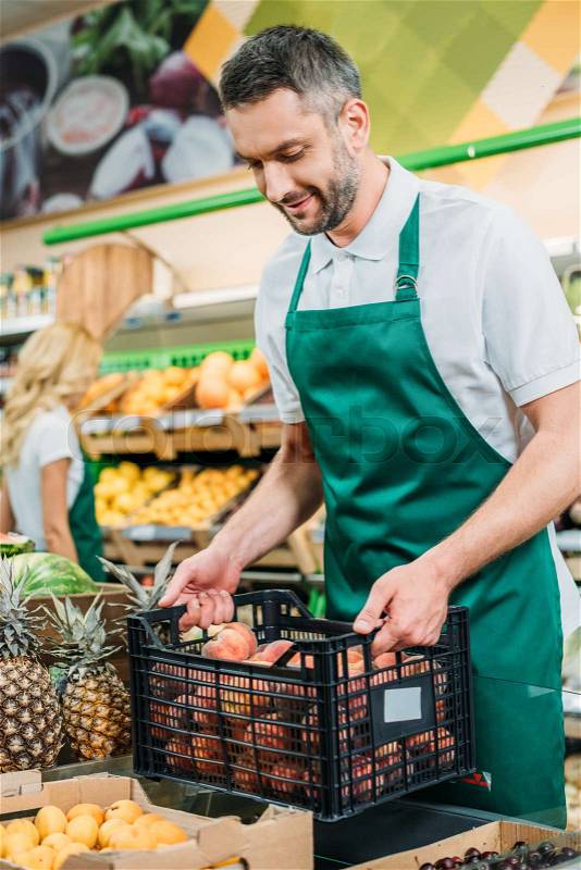 Smiling shop assistant holding basket with fruits in grocery shop, stock photo