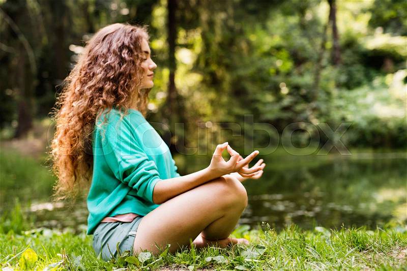 Beautiful teenage girl practices yoga in the morning forest. Young woman sits,relaxes and meditates in nature, stock photo