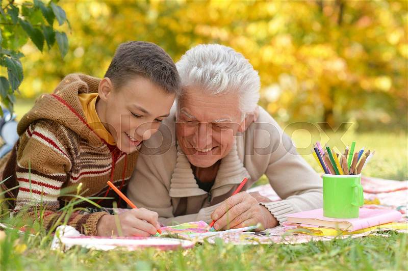 Grandfather and grandson drawing together with pencils at table, stock photo