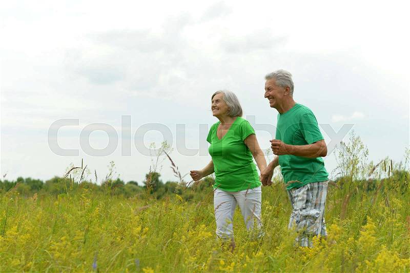 Happy senior couple running on green meadow, stock photo