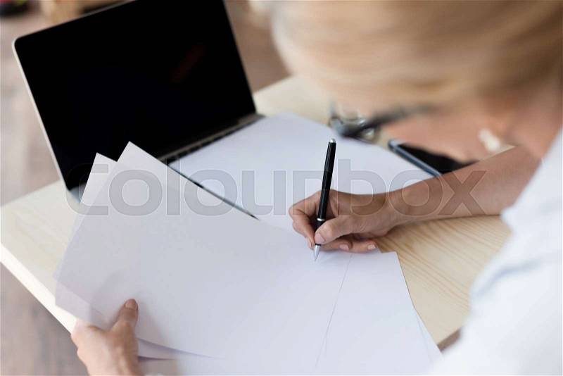 Cropped shot of businesswoman writing while working with papers, stock photo