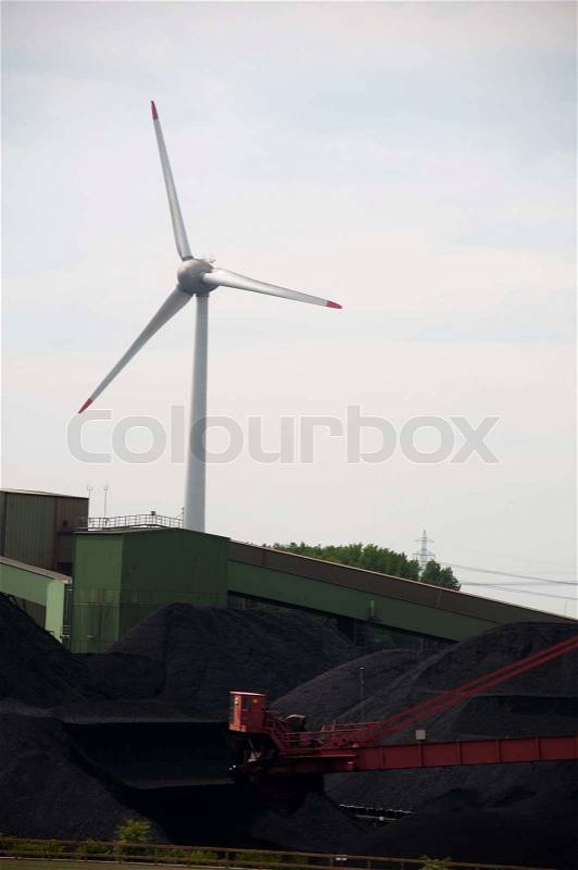 Coal storage in a factory with wind turbine in the background - conceptual, stock photo