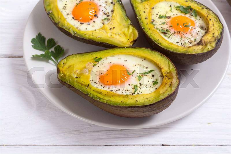 Baked avocado with eggs on woode background , stock photo