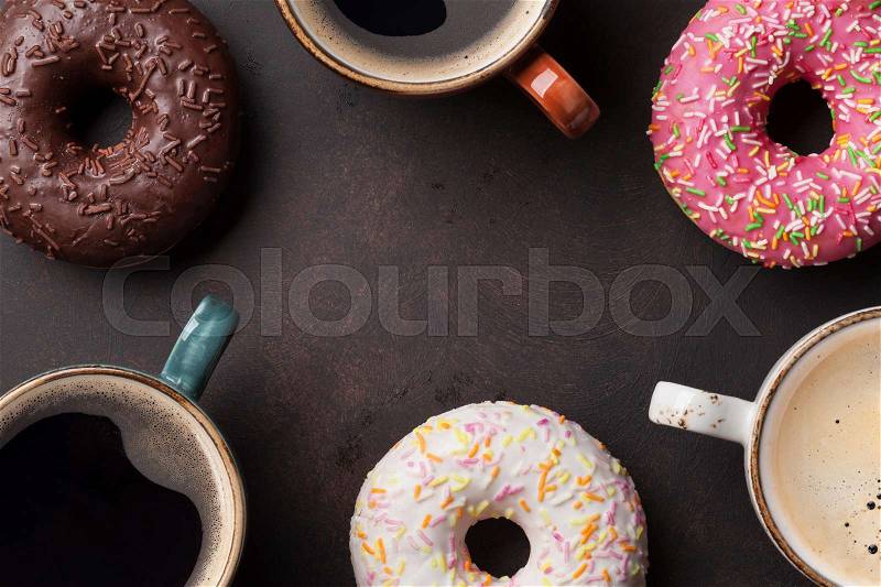 Coffee cups and colorful donuts on stone table. Top view with copy space, stock photo