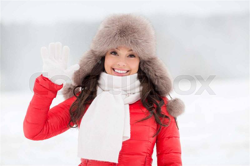 People, gesture and leisure concept - happy smiling woman in winter fur hat waving hand outdoors, stock photo