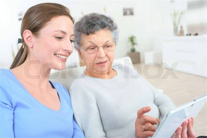 Girl teaching internet with computer tablet to grandmother, stock photo