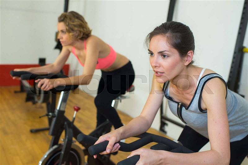 Group of women riding on exercise bike in gym, stock photo