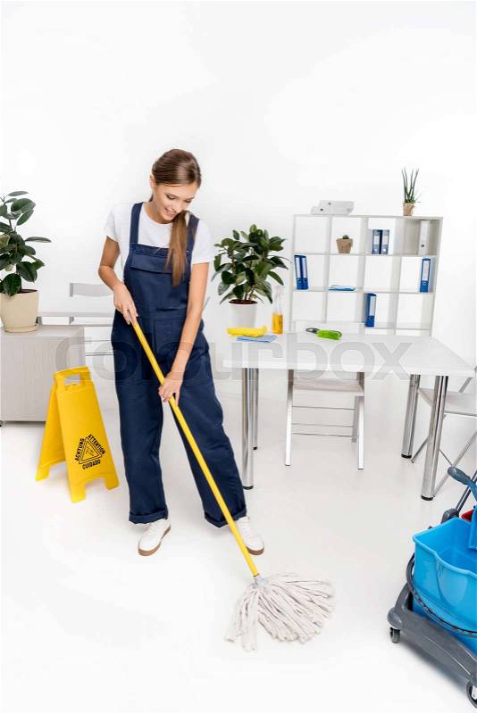 Smiling young cleaner washing floor with mop, stock photo