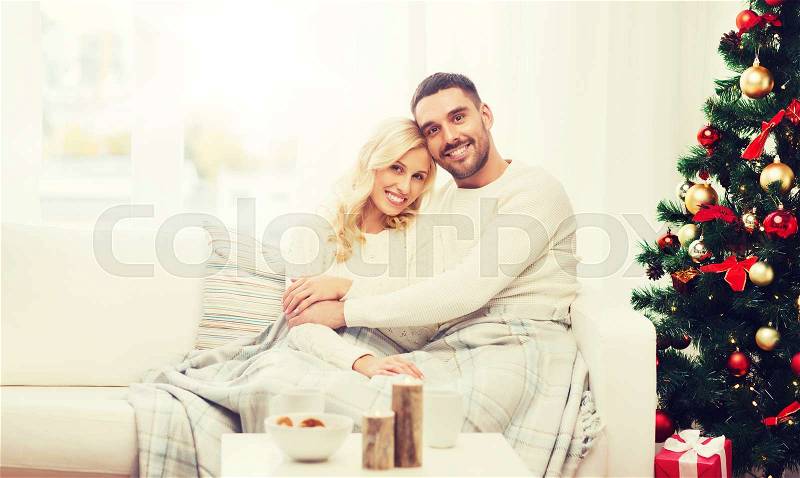 Family, christmas, holidays, love and people concept - happy couple covered with plaid sitting on sofa at home, stock photo