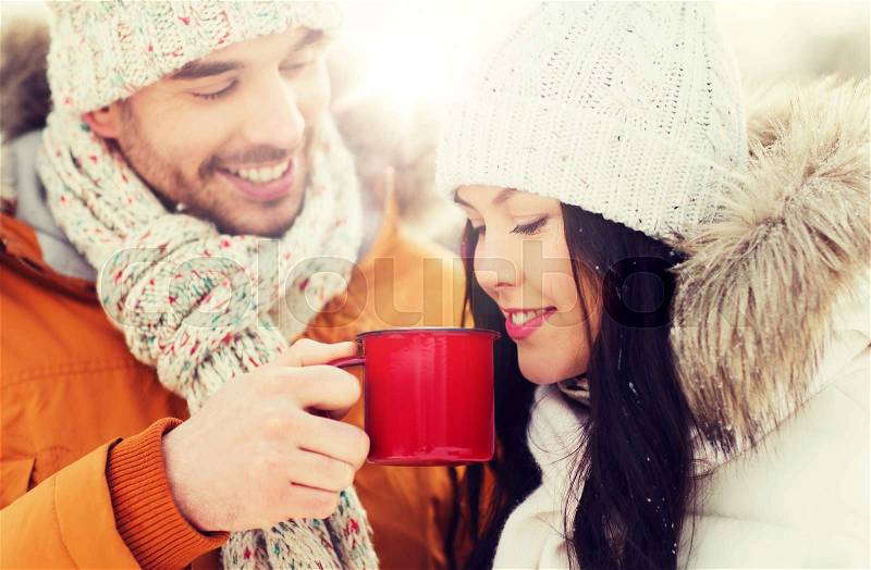 People, season, love, drinks and leisure concept - happy couple holding hot tea cups over winter landscape, stock photo