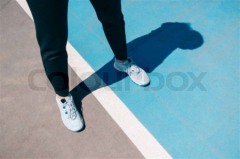 Female legs in sneakers and black sports pants on a tennis court, stock photo