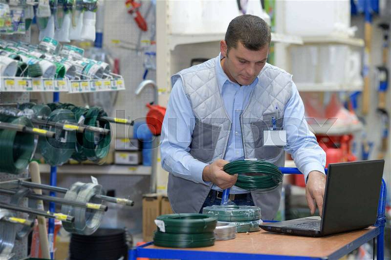 Handsome seller using laptop in hardware store, stock photo