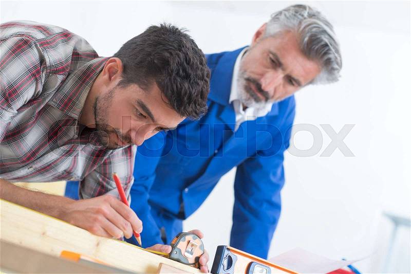 Young carpenter and his father measuring wood in workshop, stock photo