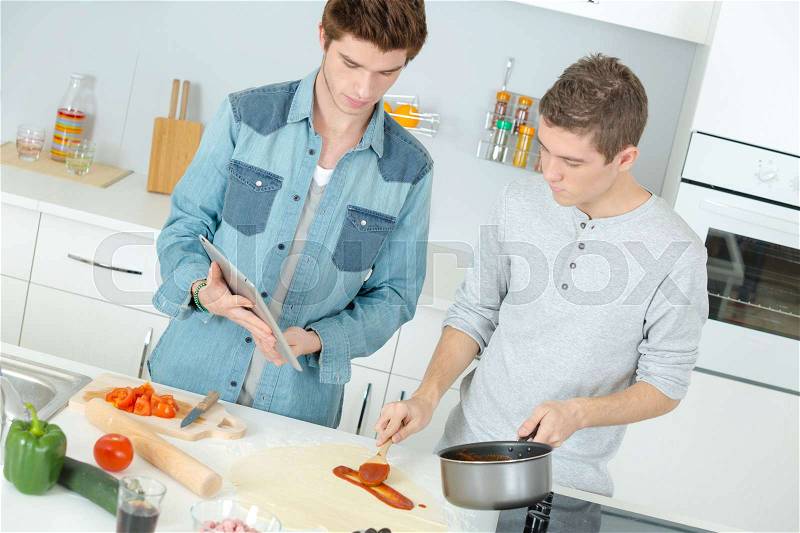 Two male friends making pizza in kitchen together, stock photo