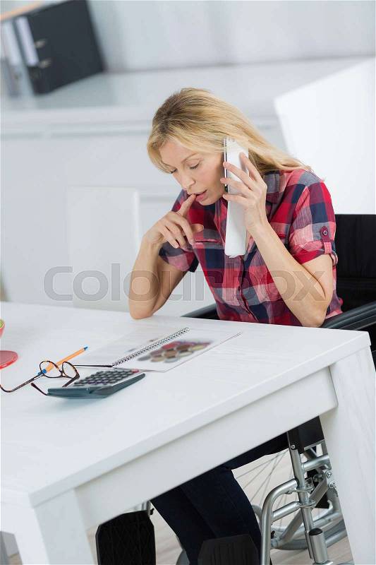 Businesswoman in wheelchair working at her desk, stock photo