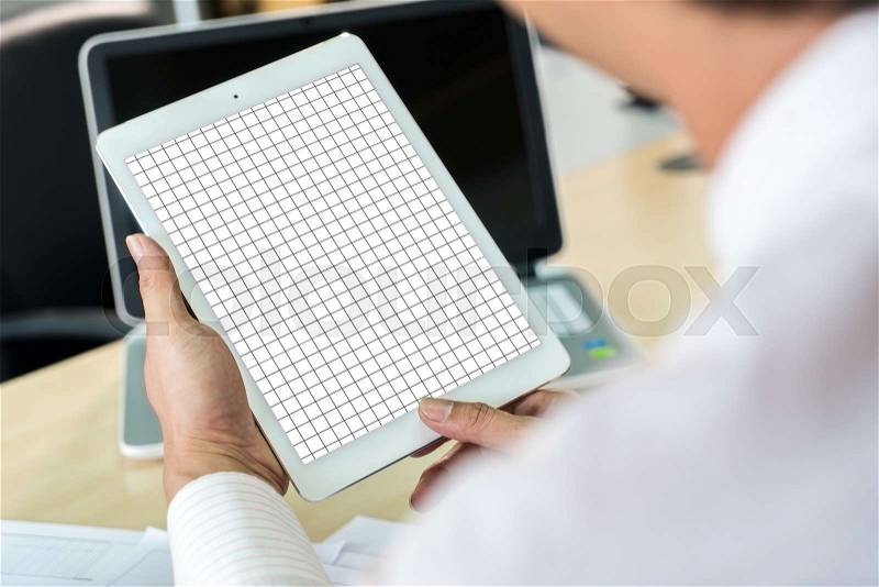 Close up the working man holding a Mock up and grid line on white tablet in hands, laptop and paper sheet of work on wooden table , stock photo