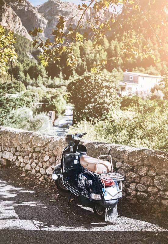 Vintage motor scooter parked at drystone wall in mediterranean landscape, stock photo