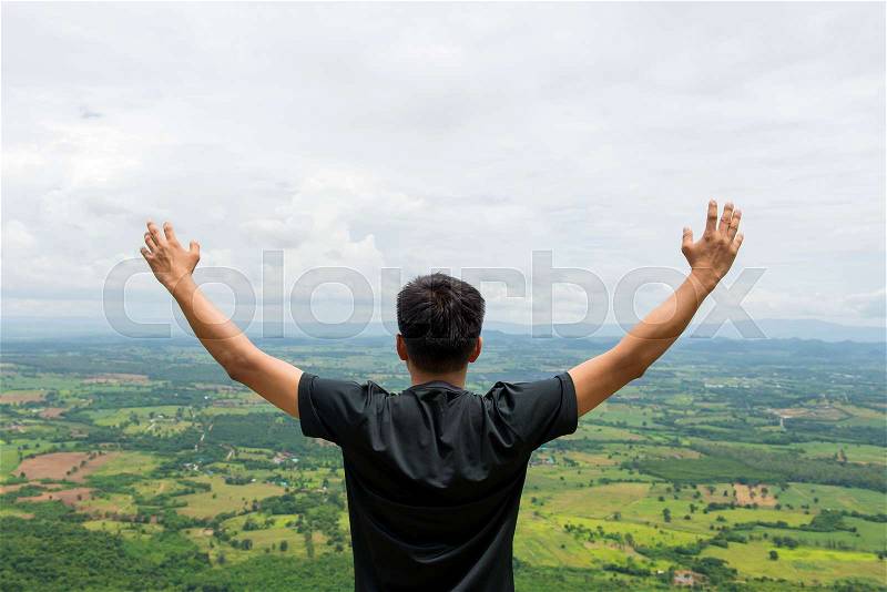 Young man standing on a mountain with raised hands and looking to view of landscape, stock photo