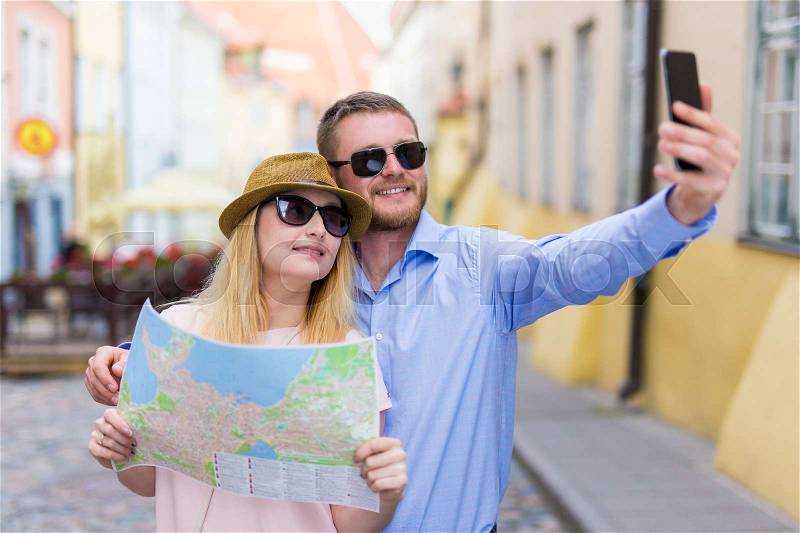 Travel and tourism concept - happy couple with city map taking photo on smart phone, stock photo
