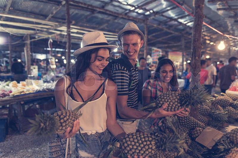 Group Of Tourists Choosing Pineapple On Tropical Street Market In Thailand Cheerful Young People Buying Fresh Fruits On Asian Bazaar, stock photo