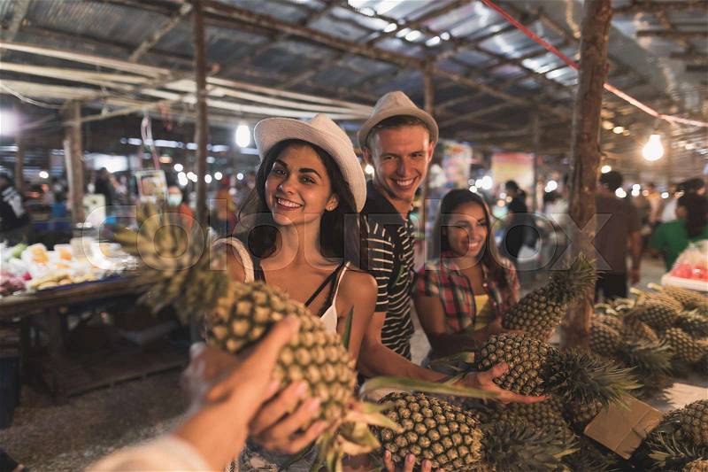 Group Of Tourists Buying Pineapple On Tropical Street Market In Thailand Young People Shopping Fresh Fruits On Asian Bazaar, stock photo