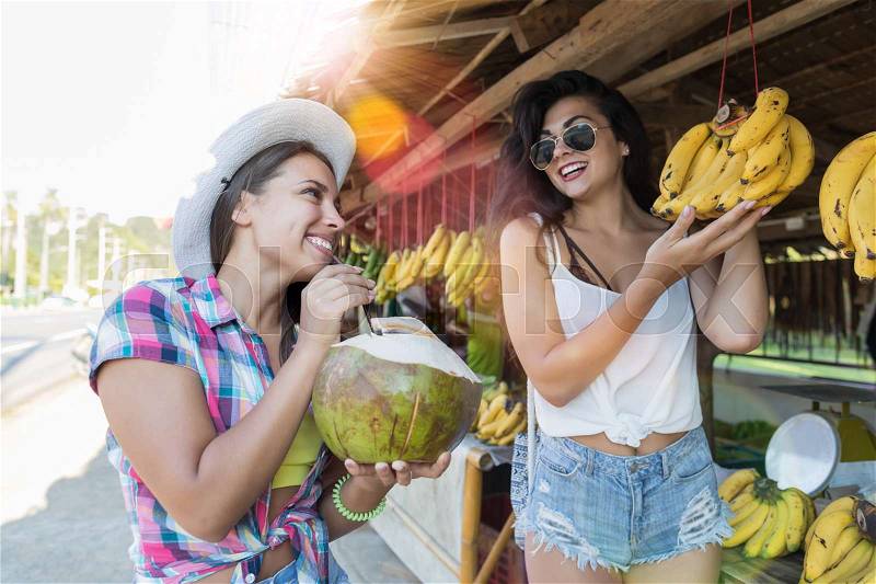 Beautiful Girls Choosing Bananas On Street Market And Drink Coconut Happy Attractive Tourists In Asian Fruit Bazaar Concept, stock photo