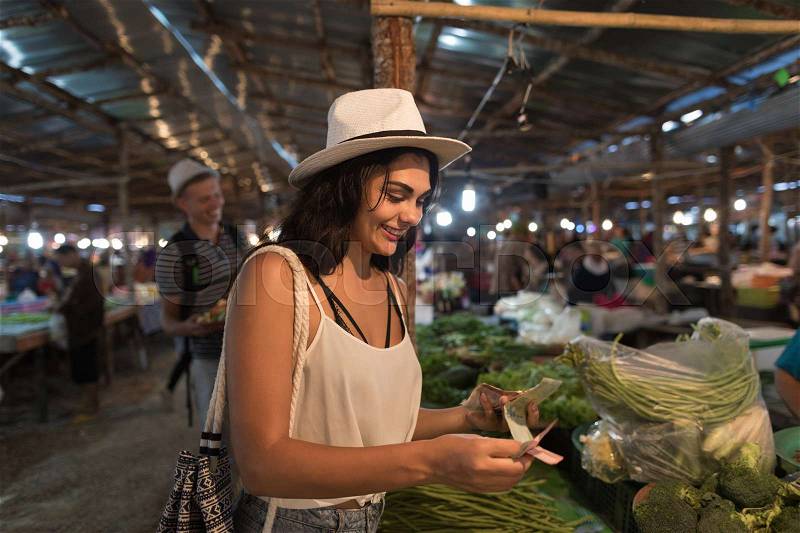 Young Woman Paying Money For Fresh Vegetables On Market Girl Shopping On Trational Street Bazaar, stock photo