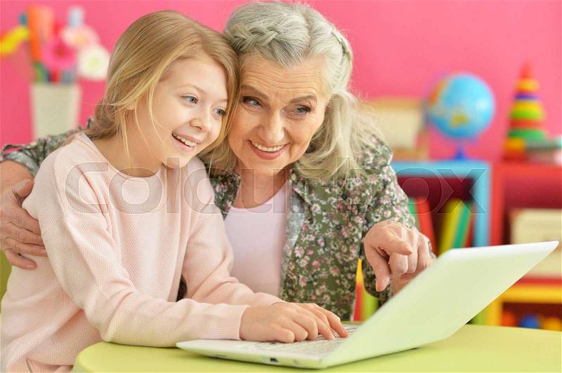 Cute little girl with her grandmother using modern laptop, stock photo