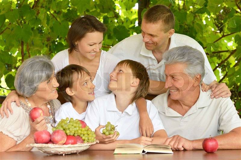 Happy parents and children at a table eating fruits in summer, stock photo