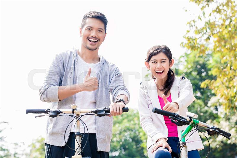 Young Asian couple laughing together while riding bicycles outdoors in summer , stock photo