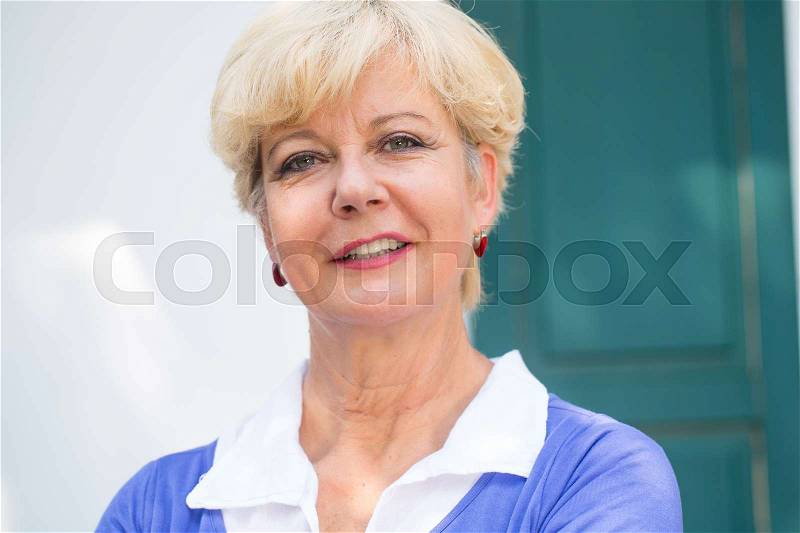 Close-up portrait of an elegant senior woman smiling while looking at camera with confidence and positive attitude outdoors, stock photo