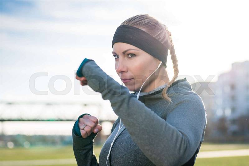 Portrait of a strong young woman practicing boxing exercise while looking forward with confidence and determination outdoors in the city, stock photo