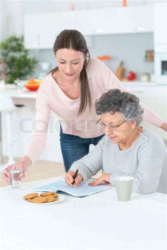 Grandmother solving crosswords puzzle helped help by her grand daughter, stock photo