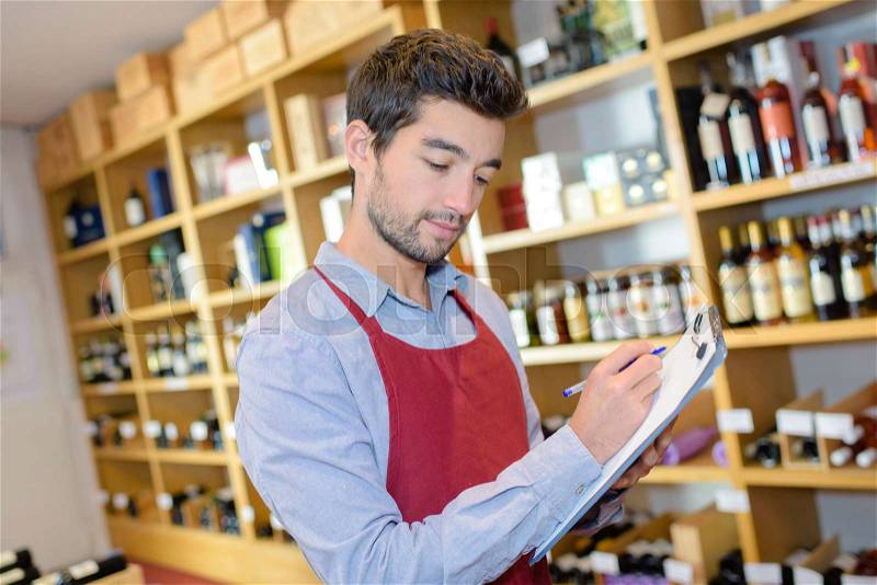 Handsome young male doing inventory at liquor store, stock photo