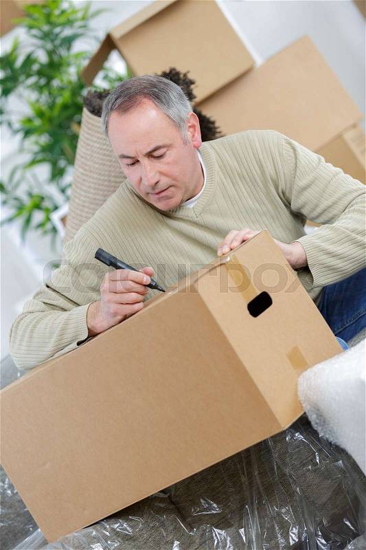 Happy man moving into new house and writing on box, stock photo