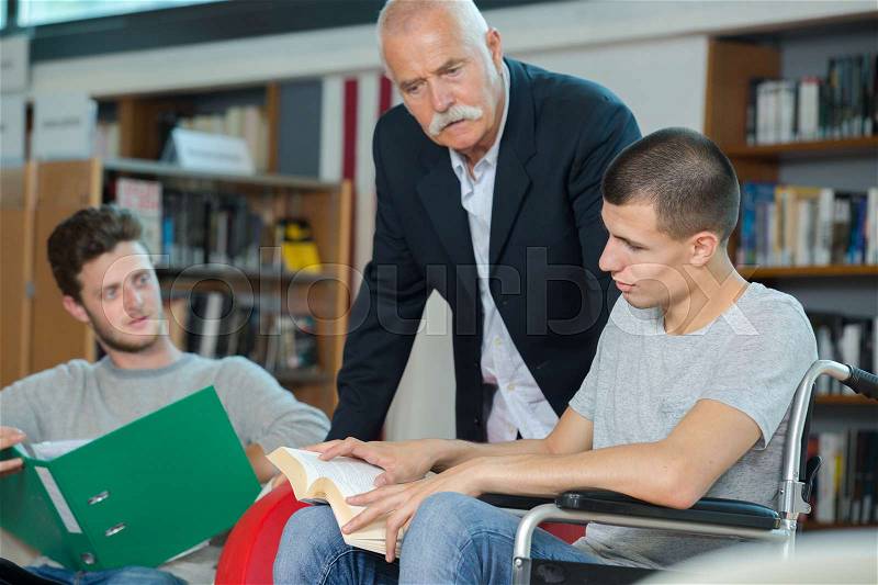 Disabled student in the school library with friend and librarian, stock photo